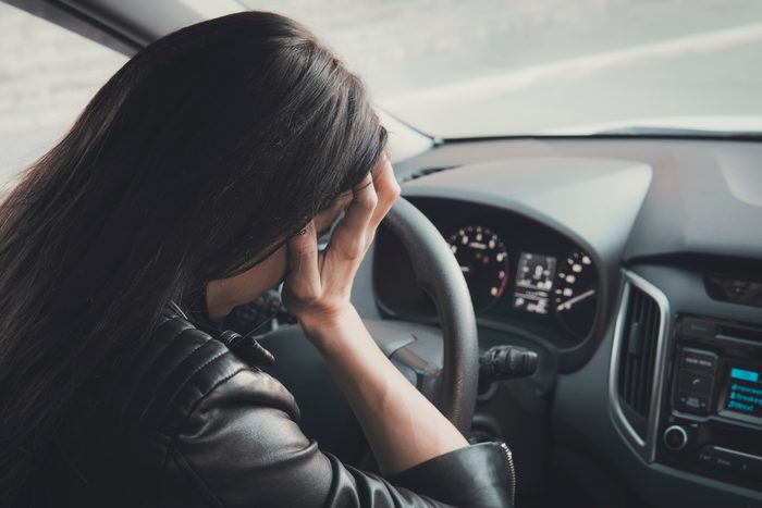 Stressed woman driver sitting inside her vehicle. Brunette girl doing face palm being at car wheel and dashboard background. Female driver is frustrated because of car accident. Headache and sickness