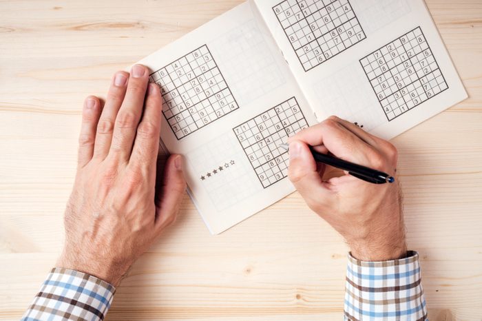 Top view of male hands solving sudoku puzzle on wooden office desk