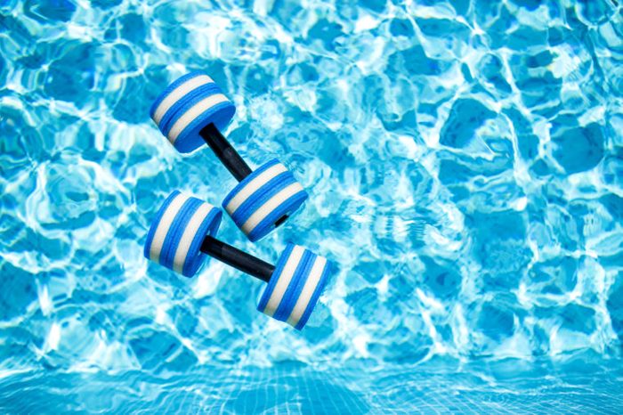 Top view of plastic dumbbells for aqua aerobics floating in blue water of swimming pool on summer day outdoors