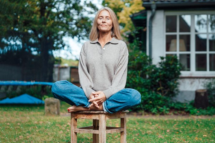 Woman practicing yoga on stool at backyard