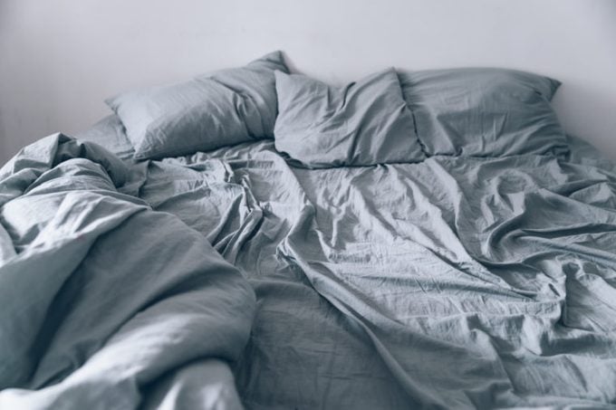 Empty messy gray bed with pillows and blanket