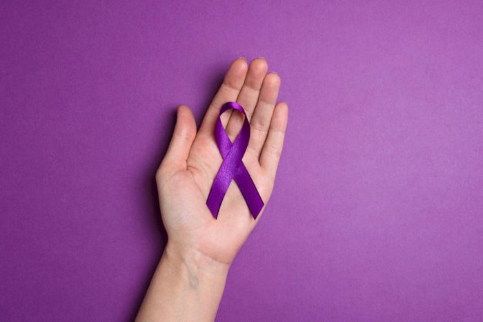 Hand holding Purple ribbons on a p urple background. World epilepsy day. Alzheimer's disease, Pancreatic cancer, Epilepsy awareness, fibromyalgia awareness.