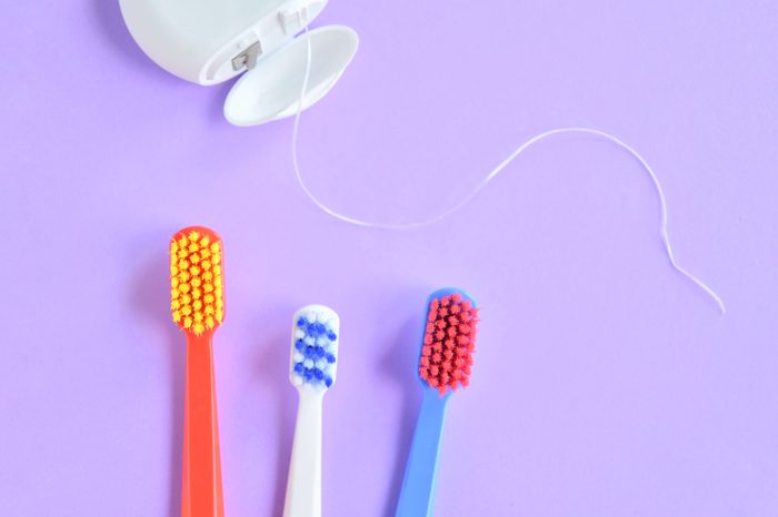 Colorful plastic toothbrushes and dental floss with selective focus on purple background with empty space for image or text. Toothbrush and hygienic dental thread for personal dental care