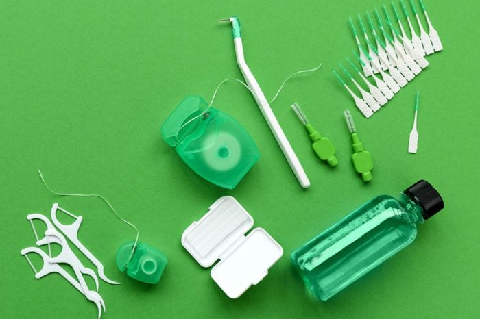 Different tools for dental care on green background. Toothbrush, cleanser, floss, flossers, wax for braces and interdental brush. Top view. Flat lay. Dental hygiene and care concept