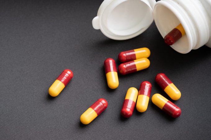 red and yellow capsules pill spilled out from white plastic bottle container. Global healthcare concept. Antibiotics drug resistance. Antimicrobial capsule pills. Pharmaceutical industry. Pharmacy.