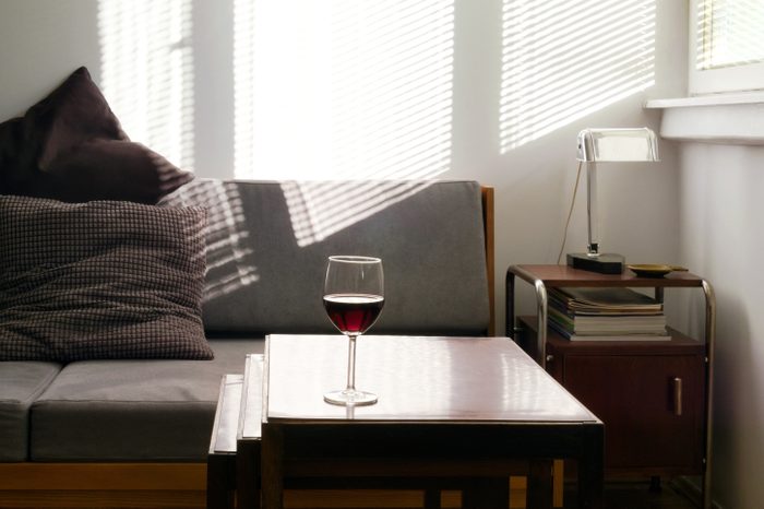Home interior with glass of red wine on nesting tables, gray sofa and light beams on wall in background