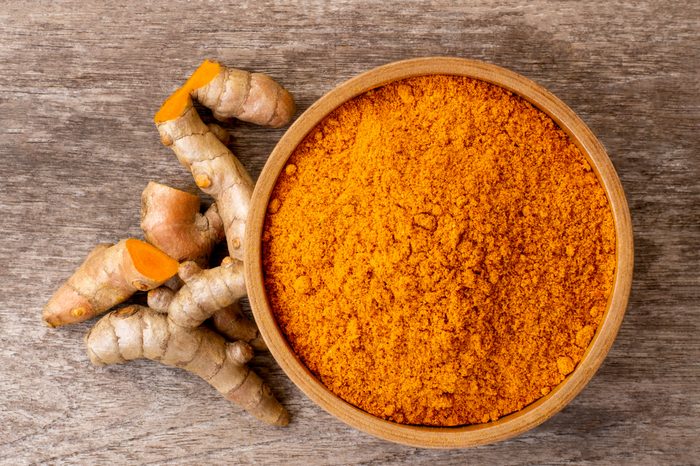 Turmeric powder in wooden bowl and tumeric root isolated on rustic wood table background. Top view. 