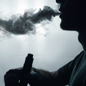 male vapor silhouette exhales a cloud of smoke using an electronic cigarette . copy space