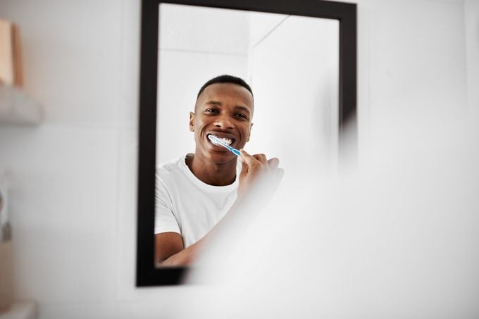 man brushing teeth in bathroom mirror