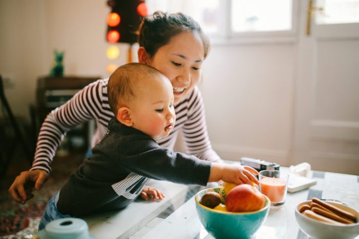 baby reaching for fruit with mother in kitchen