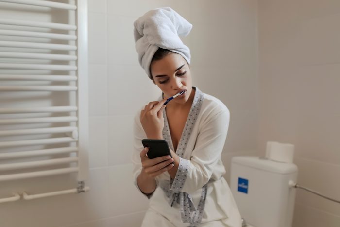 young woman brushing her teeth after shower in bathroom