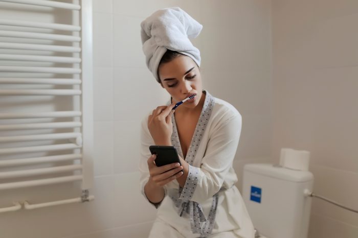 young woman brushing her teeth after shower in bathroom