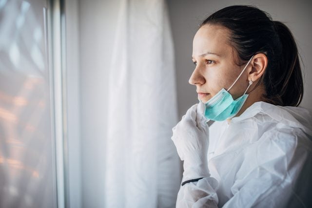 worried doctor looking out the window with gloves and mask on