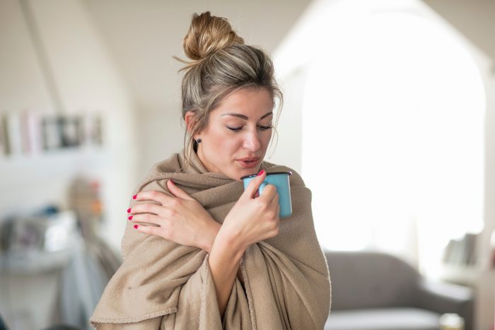 woman wrapped in blanket at home having a cup of hot tea
