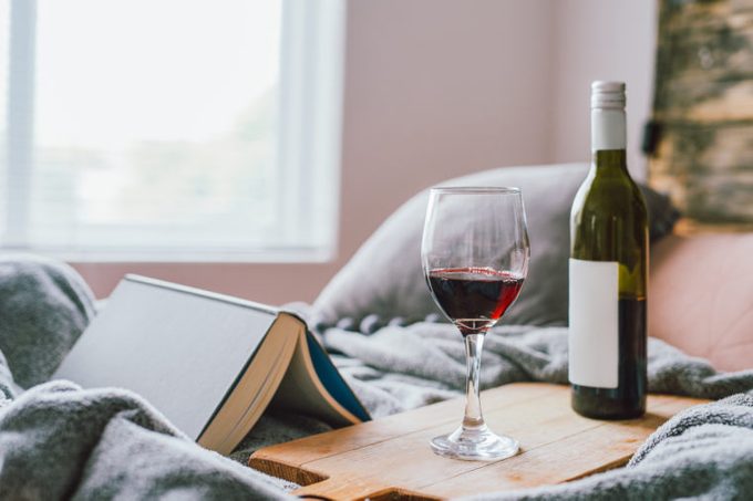 red wine bottle and glass with book on bed