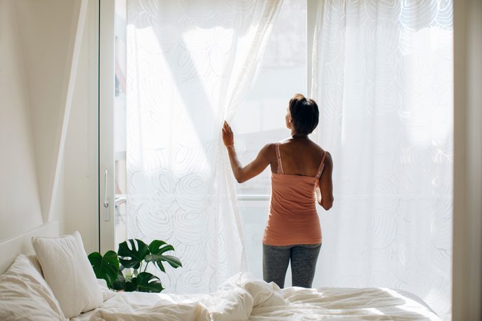 woman opening curtains and looking out window