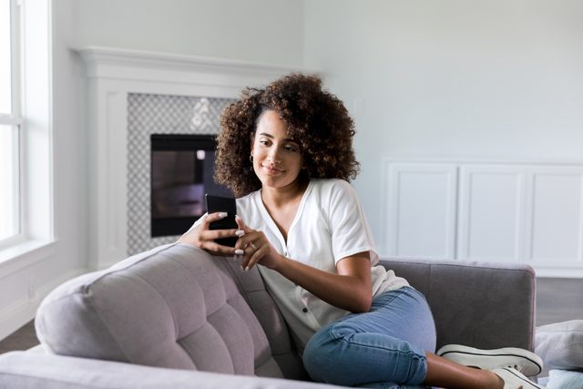 young woman sitting on couch at home looking at smartphone