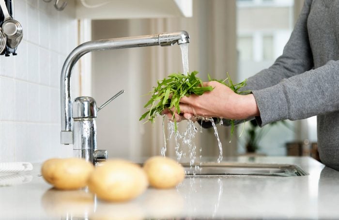 cropped shot of person cleaning produce in kitchen sink