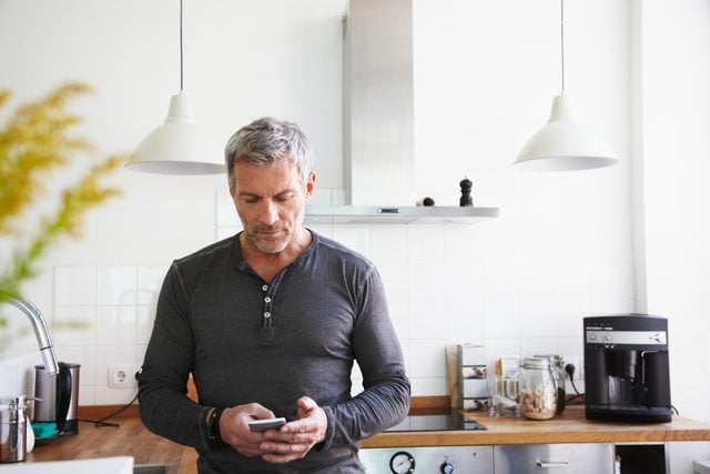man standing in kitchen looking at smartphone