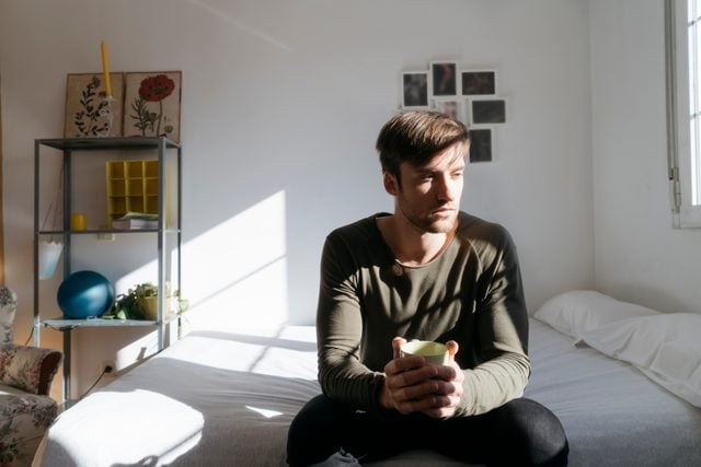 man sitting on edge of bed with coffee