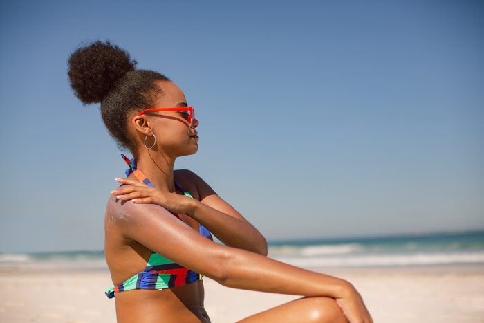 woman sitting on the beach applying sunscreen
