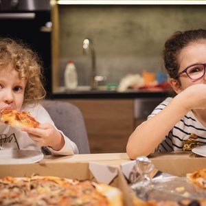 Portrait of cute little girls sitting and eating pizza