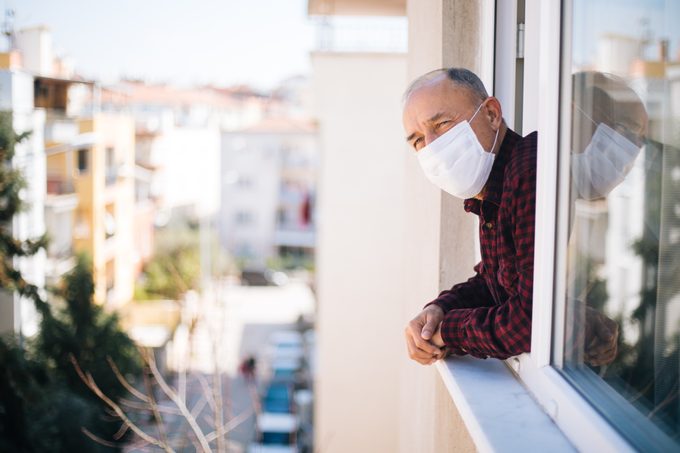 man wearing medical mask with head out of window