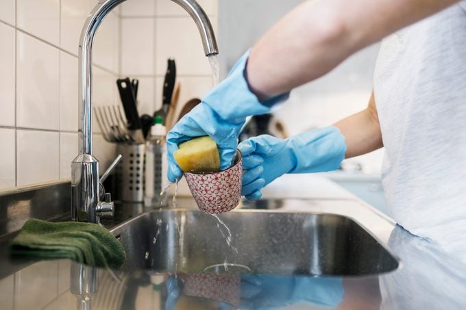 woman cleaning dish with sponge in kitchen sink