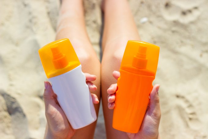 woman holding two different bottles of sunscreen on the beach