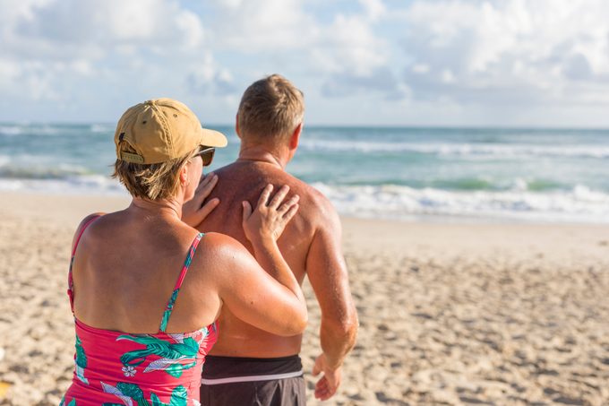 mature woman applying sunscreen to husband's back at the beach
