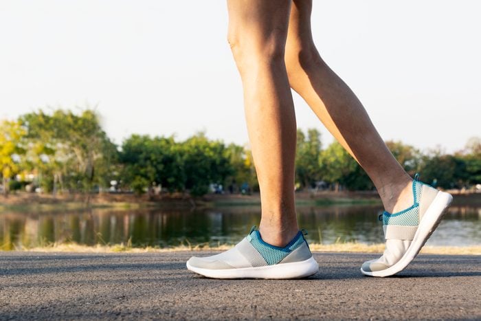 Low Section Of Woman Walking On Road Against Lake wearing slip on sneakers