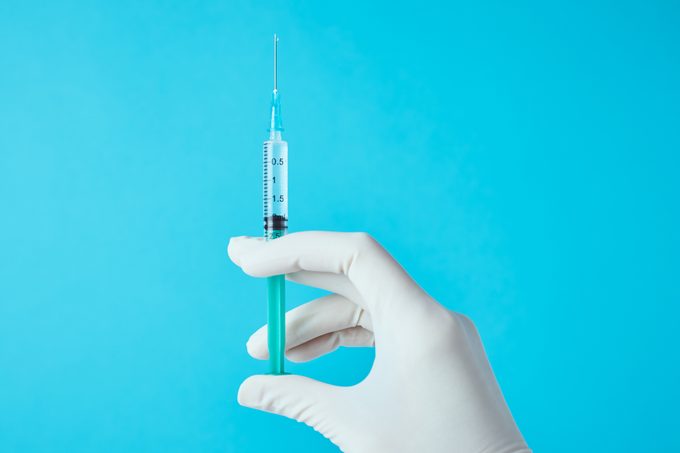 cropped shot of doctor's hand holding vaccine against blue background