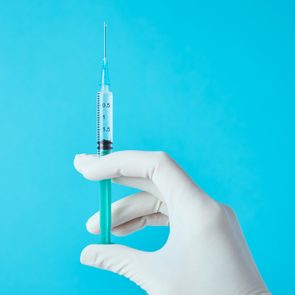 cropped shot of doctor's hand holding vaccine against blue background