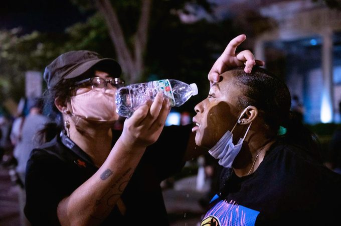 woman pouring water into another woman's eyes after being tear gassed during protest