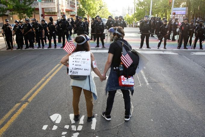 rear view shot of two protestors holding hands, american flags, and first aid kits