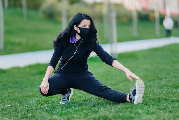 woman stretching before work out and wearing face mask protection