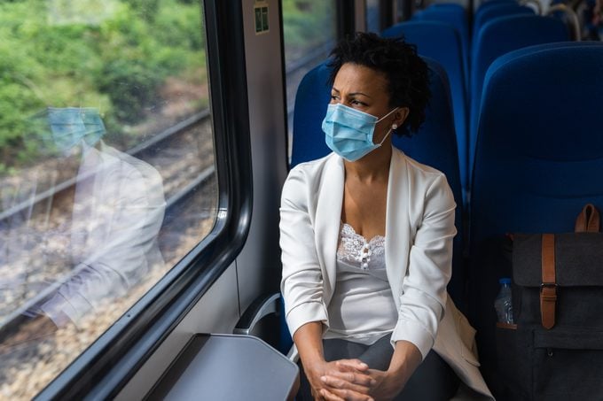 woman sitting on a train looking out the window wearing a face mask