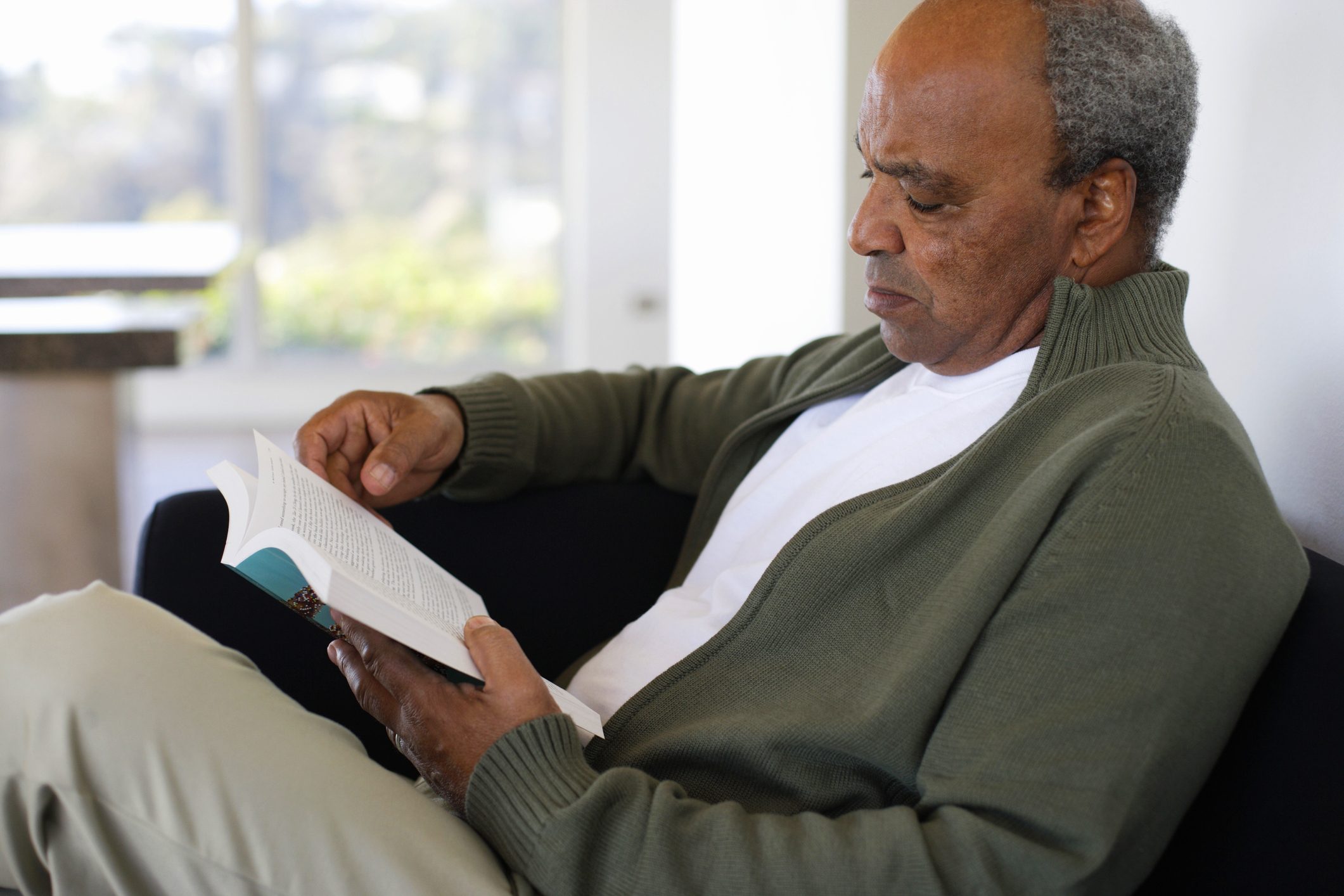 man reading a book on couch at home