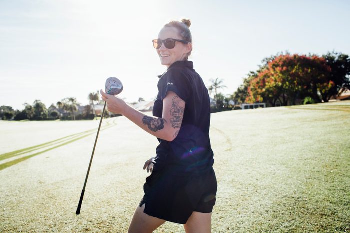 woman playing golf wearing sunglasses and smiling