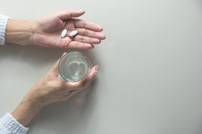overhead shot of woman's hand holding pills and glass of water