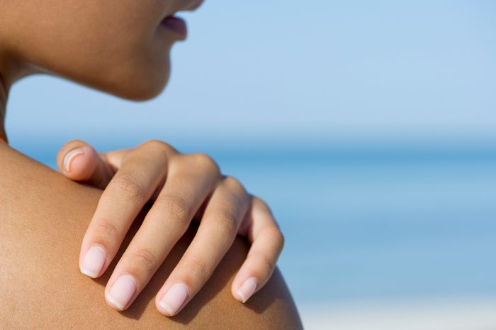 close up of woman touching her shoulder at the beach