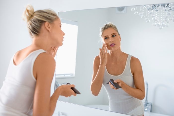woman applying self tanner on face in bathroom