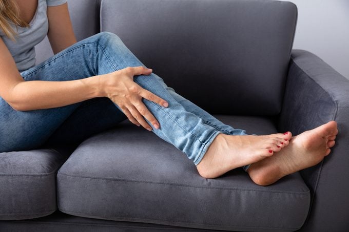 woman sitting on couch holding her leg in pain