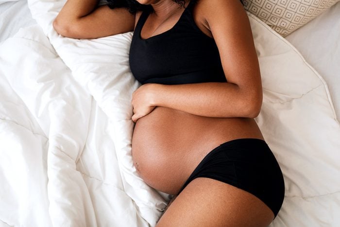 unrecognizable pregnant woman laying on a bed