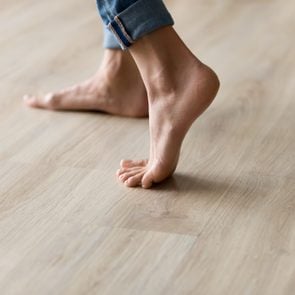 Side closeup view woman feet stands on warm wooden floor