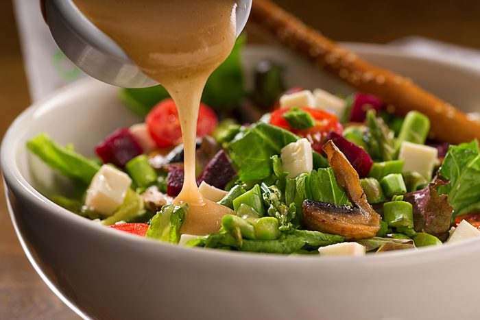 close up of dressing being poured onto salad