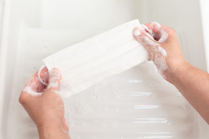 Woman's hands washing a reusable cloth face mask with soap in a white porcelain sink