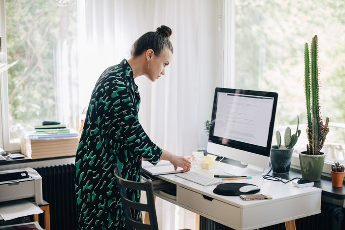 Young businesswoman reading diary while using computer monitor at desk in home office