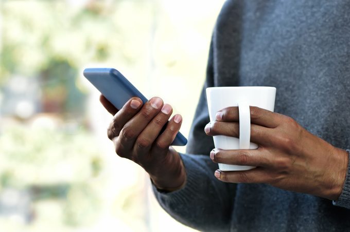 close-up van persoon met koffiemok en smartphone