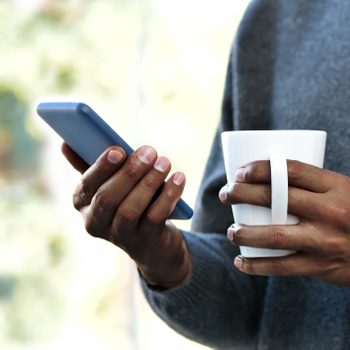 close up of person holding coffee mug and smartphone